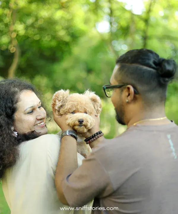 A family portrait in a lush Malaysian park, where a couple lovingly holds their poodle, showcasing the central role pets play in our lives.