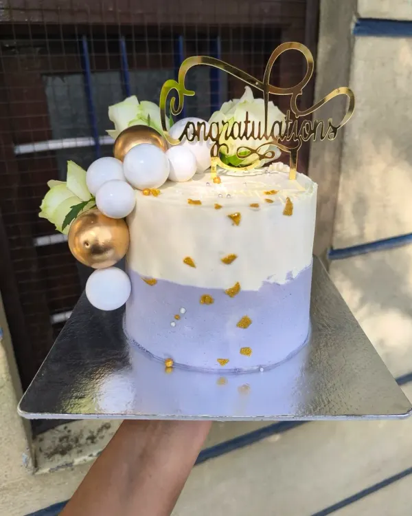 This lilac and gold cake is a dream for any elegant celebration. The combination of soft lavender buttercream, shimmering gold leaf, decorative spheres, and fresh white flowers creates a sophisticated and modern look.