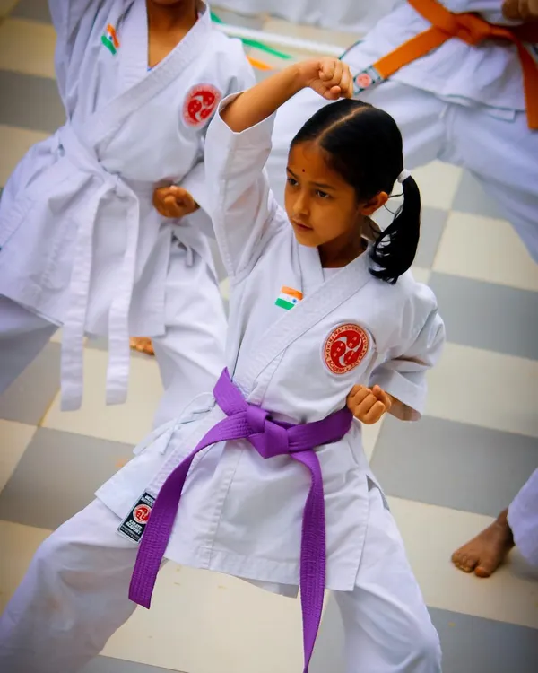 A young student demonstrates a powerful high block during an outdoor training session. Her focused expression and sharp form showcase the discipline and technical skill we instill in our karateka from an early age, building both physical strength and mental concentration.
