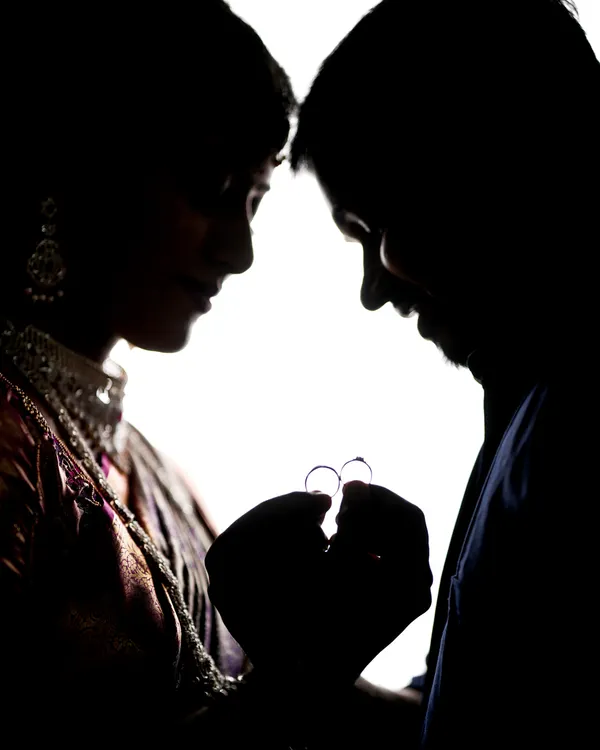 A creative silhouette shot focusing on the couple's hands as they hold their engagement rings.
