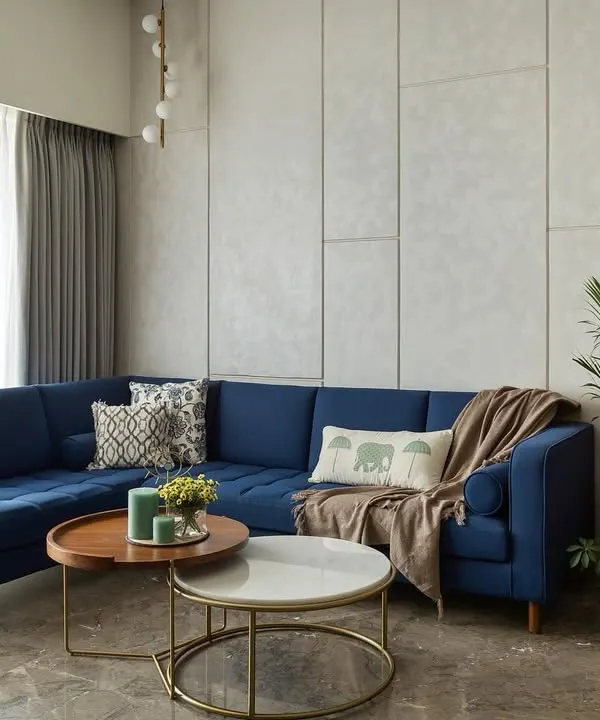 The centerpiece of the 'Top Floor Retreat' living room is this stunning, custom-made blue sectional sofa. It brings a vibrant energy to the space, balanced by the neutral grey paneled wall and layered coffee tables.