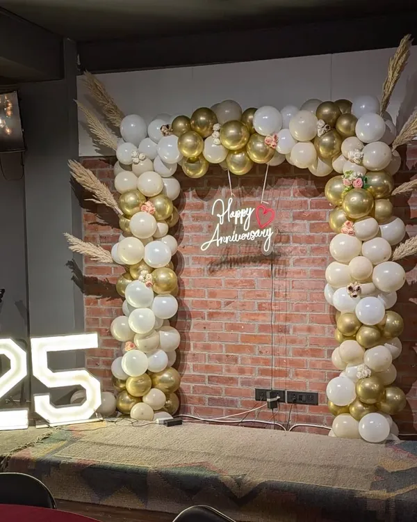 A full view of the 25th anniversary stage setup, featuring the gold and white balloon arch, 'Happy Anniversary' neon sign, and large '25' marquee numbers.