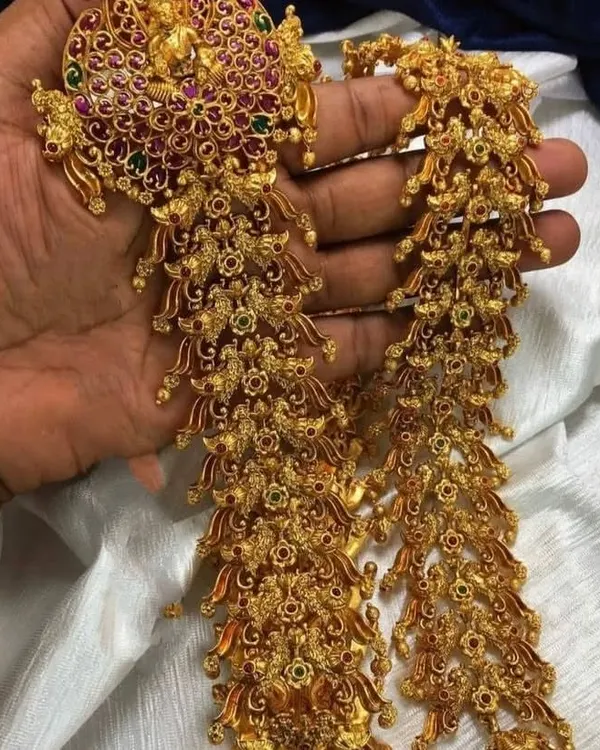 This is a traditional jade bille, a hair accessory used to decorate a long braid for a bridal look. This intricate, multi-piece ornament is available for rent to complete your muhurtham hairstyle.