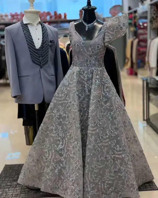 A beautiful grey gown with intricate lacework displayed next to a matching grey three-piece tuxedo. This is a perfect pairing for a reception or engagement party.