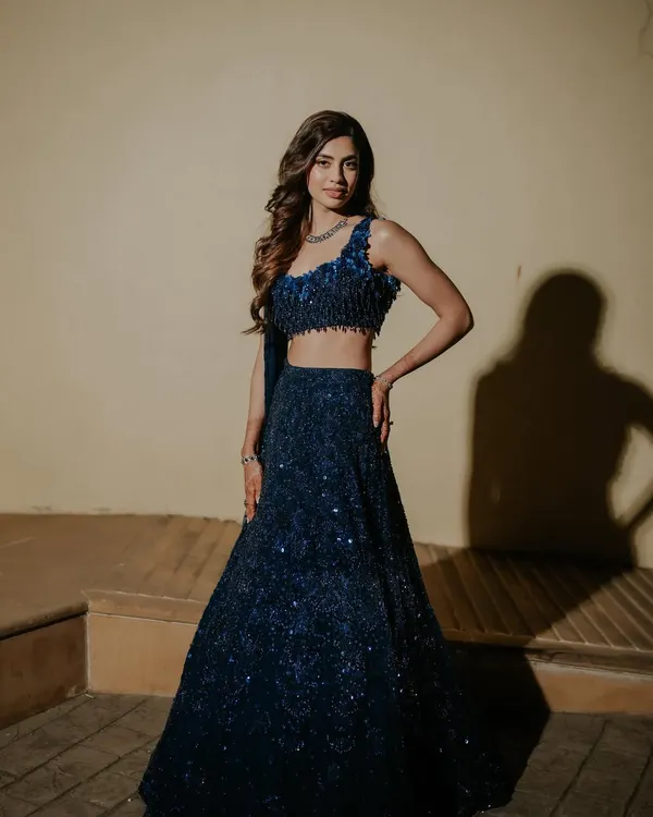 A stunning, full-length shot of the bride in her midnight blue sequined lehenga for the Sangeet. The makeup is glamorous, with a focus on the eyes, perfect for a night of dancing.