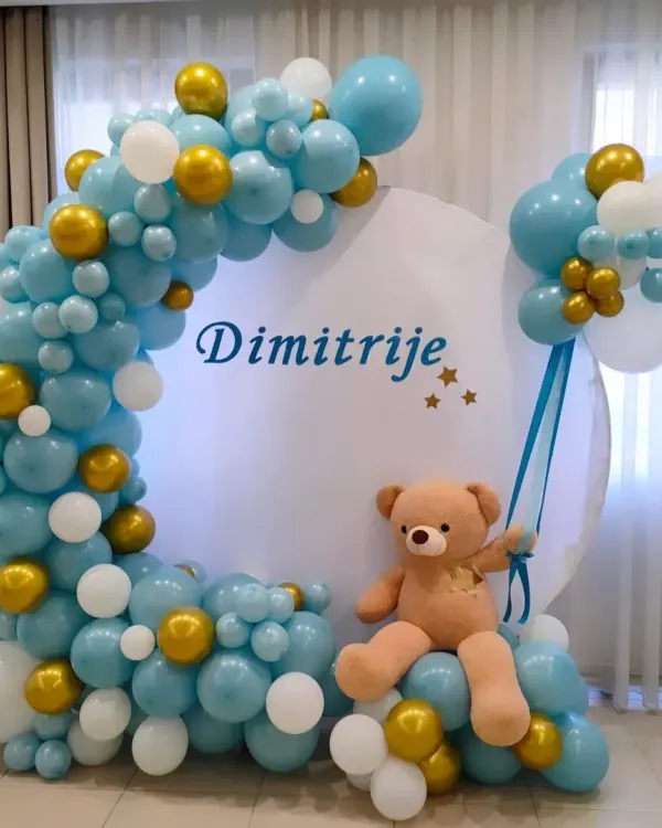 A lovely teddy bear theme for baby Dimitrije. This setup features a crescent-shaped balloon arch in blue, white, and gold around a personalized circular backdrop.