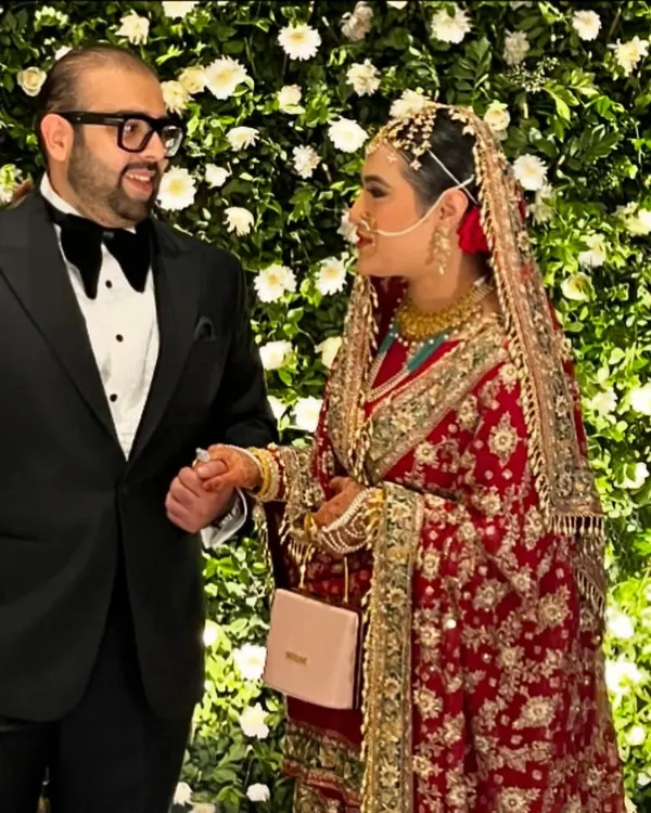 A beautiful moment between the bride and groom at their Walima reception. They are pictured against a stunning wall of white flowers, a signature of our elegant Muslim wedding decor.