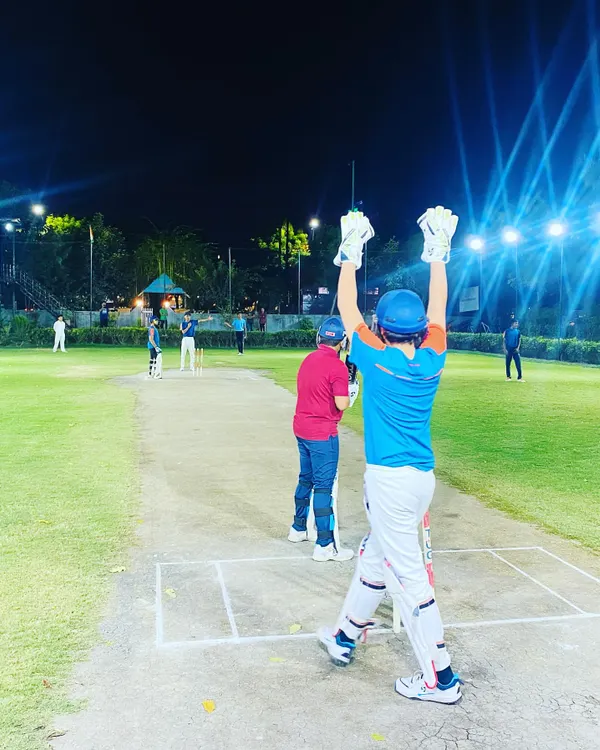 A batsman celebrates hitting the winning runs during a night match. The energy under the lights is electric, making every moment memorable.