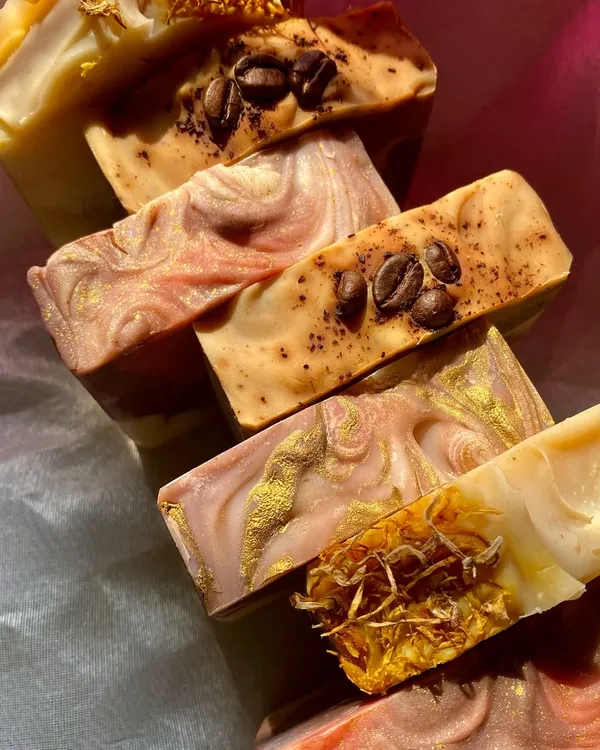 A beautiful stack showcasing the variety of our artisan soaps. You can see bars topped with coffee beans and dried calendula, and others with intricate swirls of natural clays and micas.