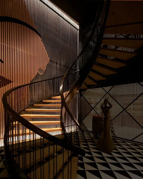 This spiral staircase is a centerpiece, where light is the primary architectural material. I used a technique called wall grazing, with linear fixtures at both the ceiling and floor, to cast dramatic shadows and highlight the texture of the vertical slats, transforming a simple passage into a powerful visual journey.