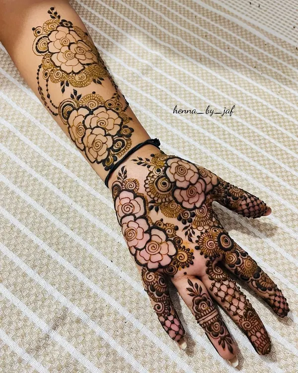 A full bridal mehndi design covering the entire hand and extending up the arm. This intricate piece features a dense pattern of roses, spirals, and detailed shading, with delicate work on the fingers.