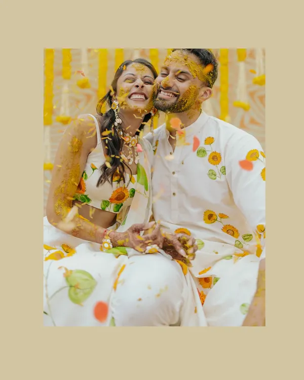 The pure joy of a Haldi ceremony. This candid shot of the couple, covered in turmeric and flowers, is full of laughter and love.