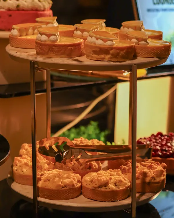 A two-tiered stand showcasing an array of our dessert offerings, including delicate lemon meringue tarts and rustic apple crumbles. There is a sweet for every tooth.