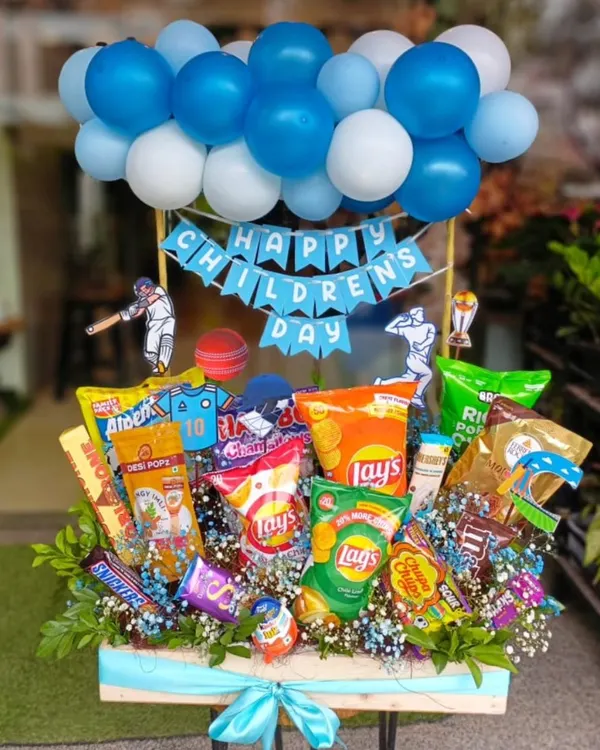 This large Children's Day hamper is packed with fun and flavor. It features a variety of chips, chocolates, and snacks, all topped with a festive balloon arrangement and cricket-themed cutouts, making it a perfect surprise for the little ones.