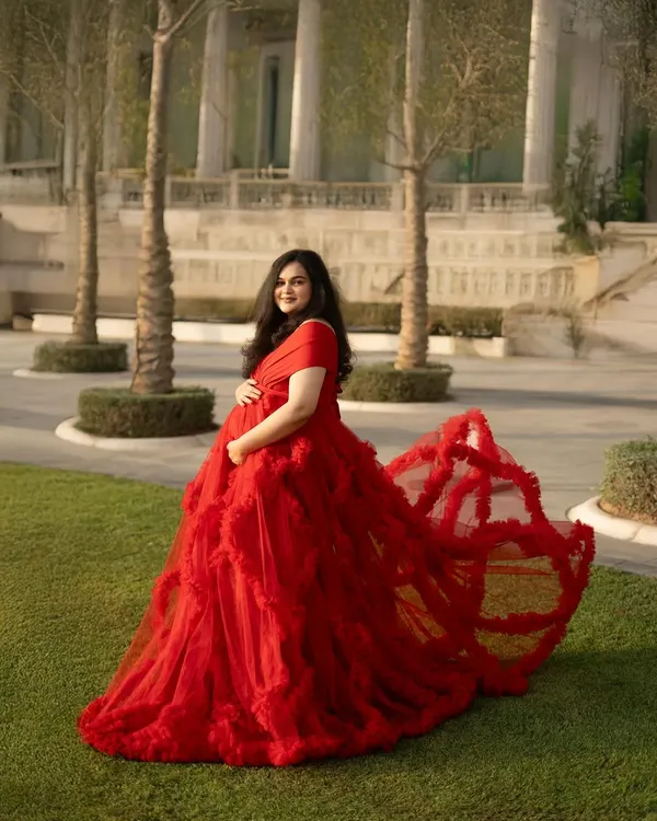 This dramatic shot showcases the incredible train of the red gown against a manicured green lawn and grand architecture. It’s a perfect blend of natural beauty and high-fashion elegance for an outdoor maternity shoot.