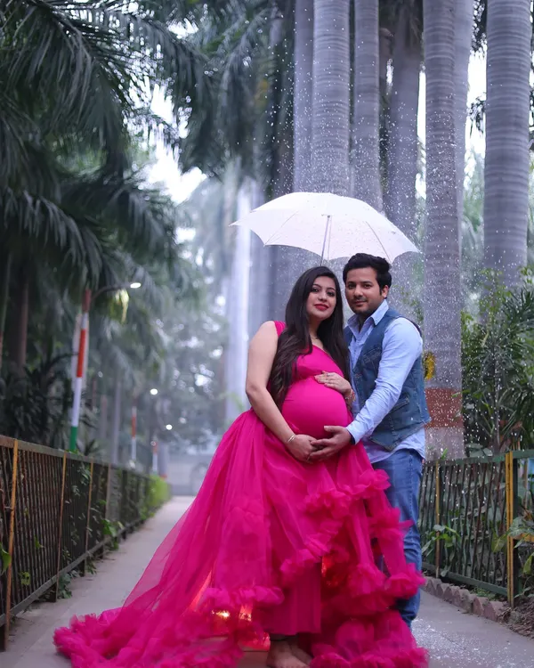 A romantic outdoor couple's portrait in a park setting. The mother-to-be's vibrant pink gown stands out beautifully against the greenery.