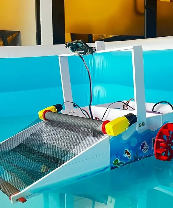 A close-up of the AI-powered river cleaning robot, showing the conveyor belt collection system, paddle wheel for propulsion, and the mounted AI camera that serves as the robot's "eyes."