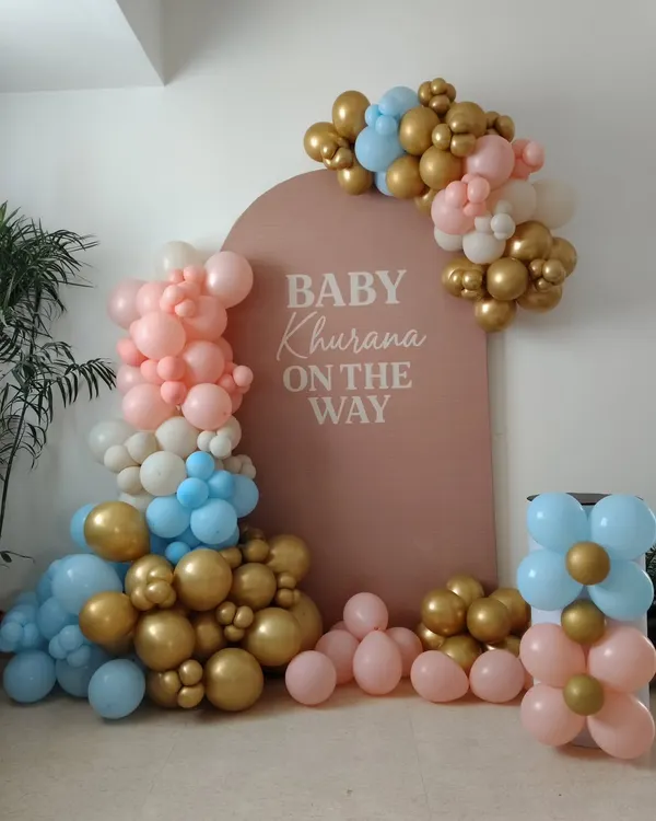 This is a popular setup for a gender reveal party, featuring a 'Baby on the Way' backdrop personalized with the family name. The balloon arrangement uses a mix of pink, blue, and metallic gold to build anticipation for the big announcement.