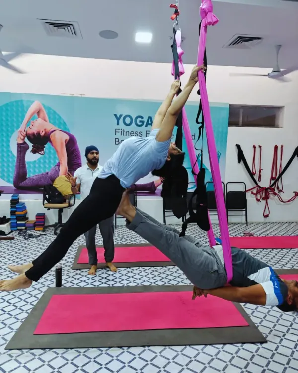 Two students work together in a partner aerial pose, using the hammock for support. This demonstrates how aerial yoga can also incorporate elements of Acro Yoga, building trust and synchronized movement.