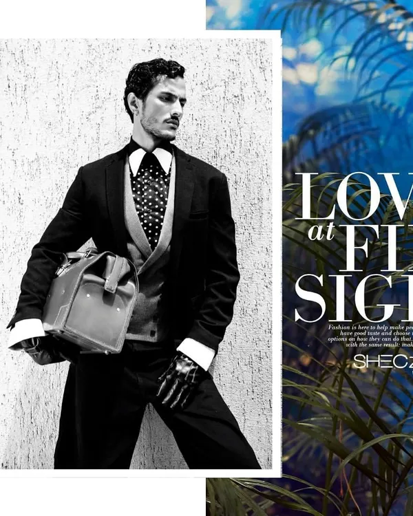 A black and white editorial shot featuring a sharply tailored three-piece suit with a polka-dot tie. The styling, complete with a vintage doctor's bag and skeleton-printed gloves, creates a narrative of a modern-day gentleman with a mysterious edge.