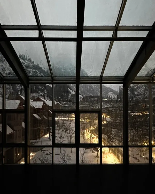 A view from within the Hamsa Resort in Manali on a winter evening. The steel-framed glass enclosure provides an uninterrupted connection to the snow-covered landscape, blending the boundary between the interior and the Himalayan outdoors.
