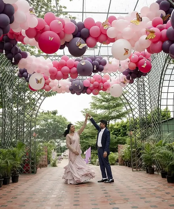 A couple dances under a spectacular balloon archway at a celebration. The vibrant pink and purple balloons create a fun and festive pathway, perfect for a milestone birthday or anniversary party.