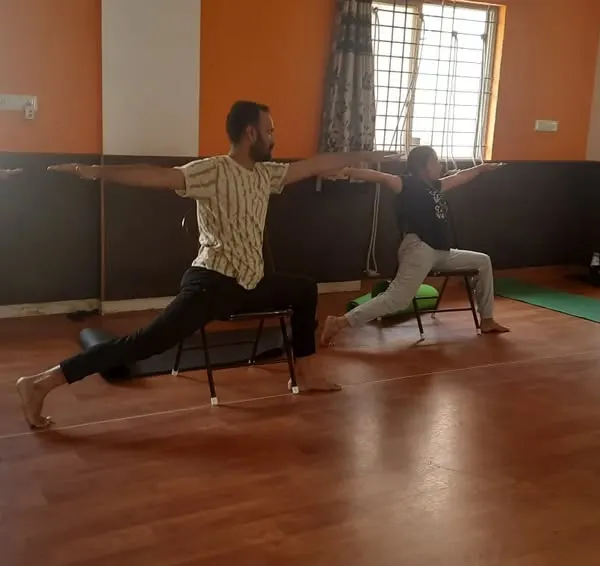 A class practices a supported Virabhadrasana (Warrior Pose) using chairs. This modification helps build strength and stability without putting pressure on the knees, making it ideal for a diverse group of employees.