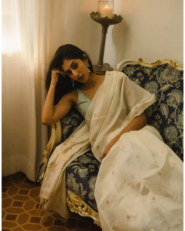 A moody and elegant portrait of a model in a beautiful white saree. The setting and lighting create a feeling of quiet contemplation.
