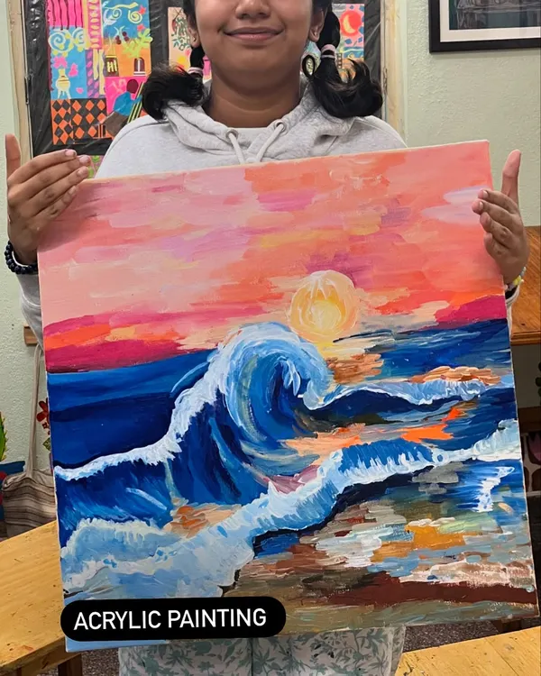 A young artist proudly presents her dynamic acrylic painting of a wave at sunset. Our classes encourage bold colors and expressive brushwork.
