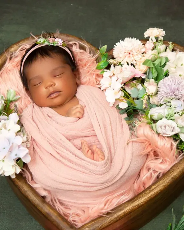 This classic newborn portrait captures a baby sleeping peacefully in a heart-shaped wooden bowl, surrounded by a bed of soft pink fur and delicate flowers. This style emphasizes your baby's serene and angelic features.