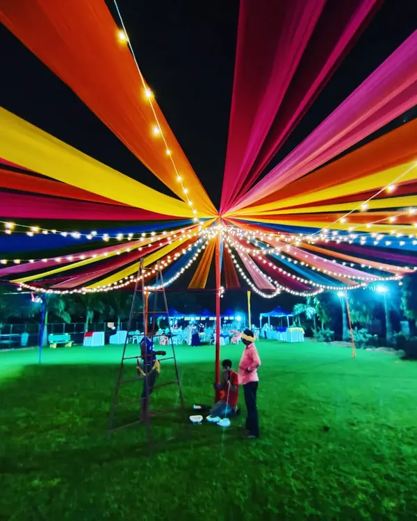 We create stunning, large-scale decorations like this vibrant, multi-colored fabric canopy for a Dandiya night. The structure is illuminated with strings of fairy lights, creating a festive and immersive atmosphere for hundreds of guests on a large community lawn.