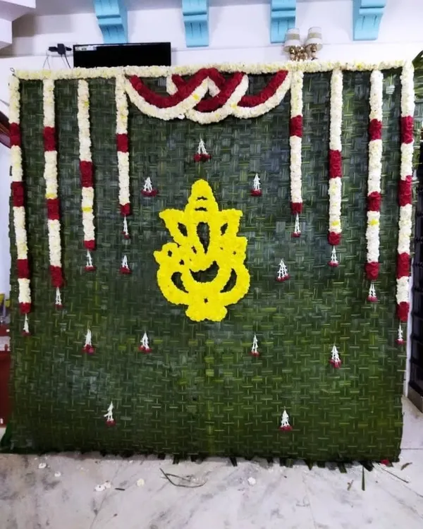 I create unique, natural backdrops for poojas, such as this wall made of fresh banana leaves featuring a Ganesha motif crafted from yellow flowers.