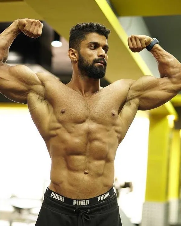 A classic front double biceps pose, showcasing arm development, chest fullness, and a tightly defined midsection. This is a foundational pose in competitive bodybuilding.