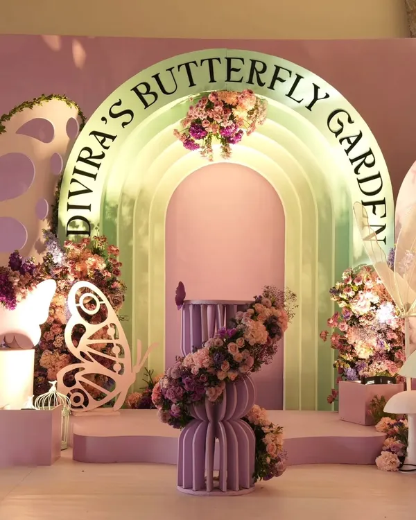 A breathtaking main stage for "Divira's Butterfly Garden" party. This luxury setup features a multi-layered arched backdrop in pastel green and pink, custom lettering, and cascading floral arrangements to create an enchanted garden atmosphere.