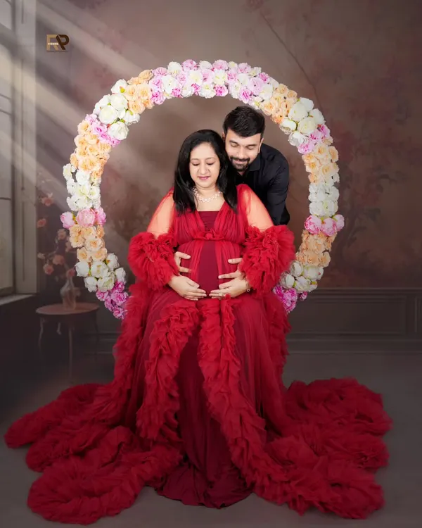 A classic pose with a modern twist. The mom-to-be is seated in a floral hoop, wearing a dramatic red gown, creating a portrait that is both romantic and powerful.