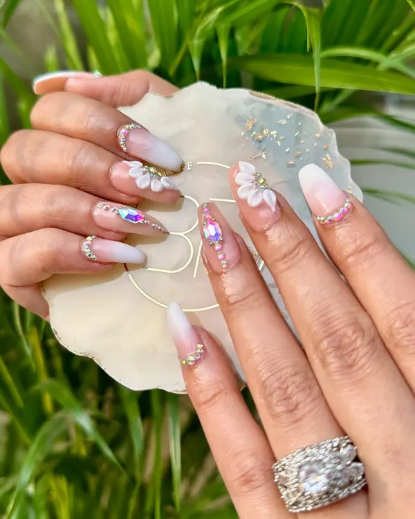Step into a garden of elegance with these 3D floral and stone nails. This bridal set features a soft ombré base, hand-sculpted white flowers, and carefully placed iridescent stones.