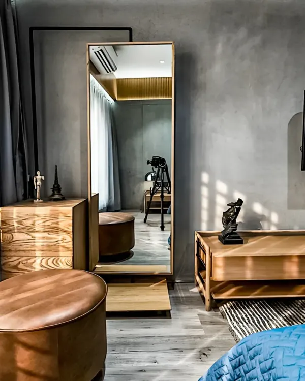 This bedroom corner is designed for getting ready in style, with a full-length mirror, a wooden dresser, and comfortable leather ottomans. The concrete-finish wall adds an industrial-chic touch to the warm and inviting space.