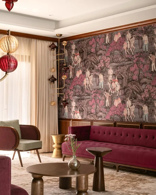 A living room where curated maximalism comes to life. A deep magenta sofa and a statement wallpaper depicting a historical scene create a rich, narrative-driven backdrop, complemented by unique, sculptural lighting fixtures.