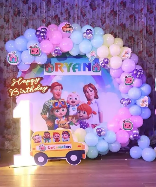 A complete Cocomelon theme for a first birthday party. This setup features a balloon arch in pastel colors, a custom backdrop with the whole Cocomelon family, and character standees.