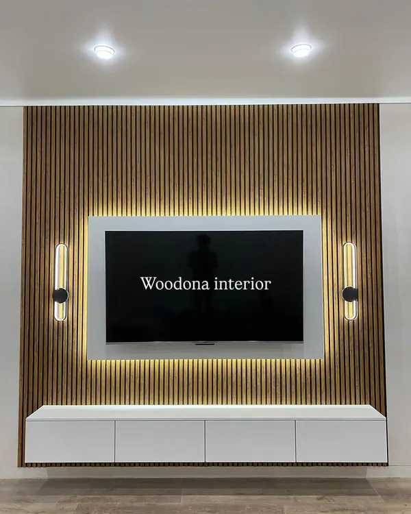 A beautiful TV unit design featuring a fluted wood panel background. The floating white console, backlit TV panel, and stylish wall sconces create a modern and elegant look.