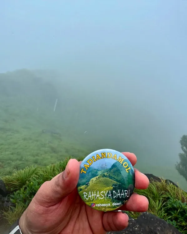 Our Tadiandamol trek badge, held against the misty hills of Coorg. This trek takes you to the highest peak in the Kodagu district.