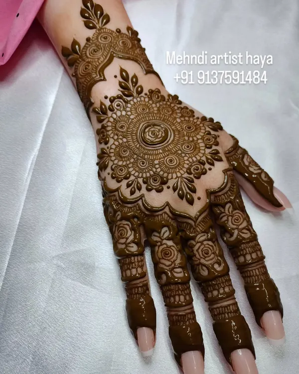 A classic bridal design featuring a large, intricate mandala on the back of the hand. The fingers are adorned with matching detailed patterns, creating a cohesive and traditional look.