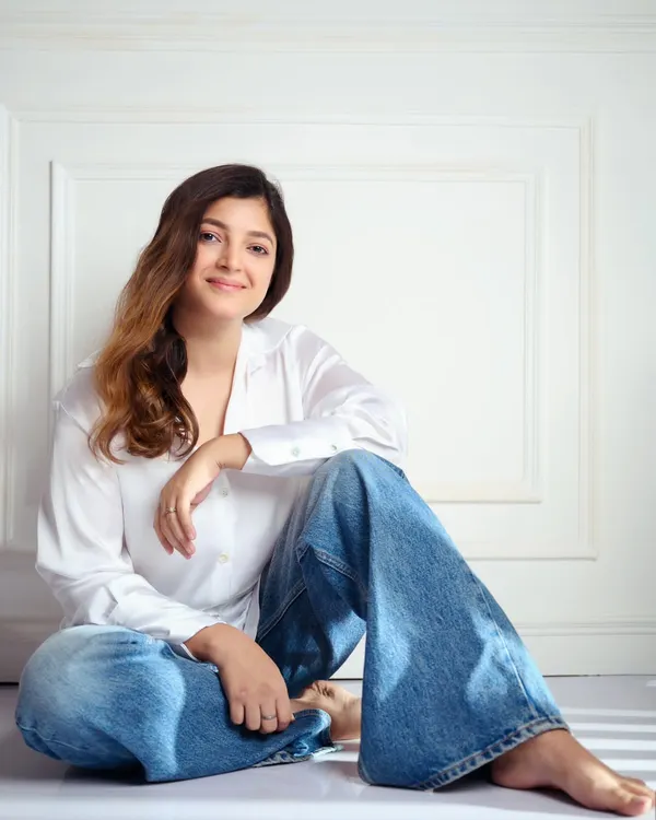 A natural light portrait of a model against a clean white background. The relaxed, seated pose and gentle smile create a warm and approachable headshot, perfect for a portfolio.