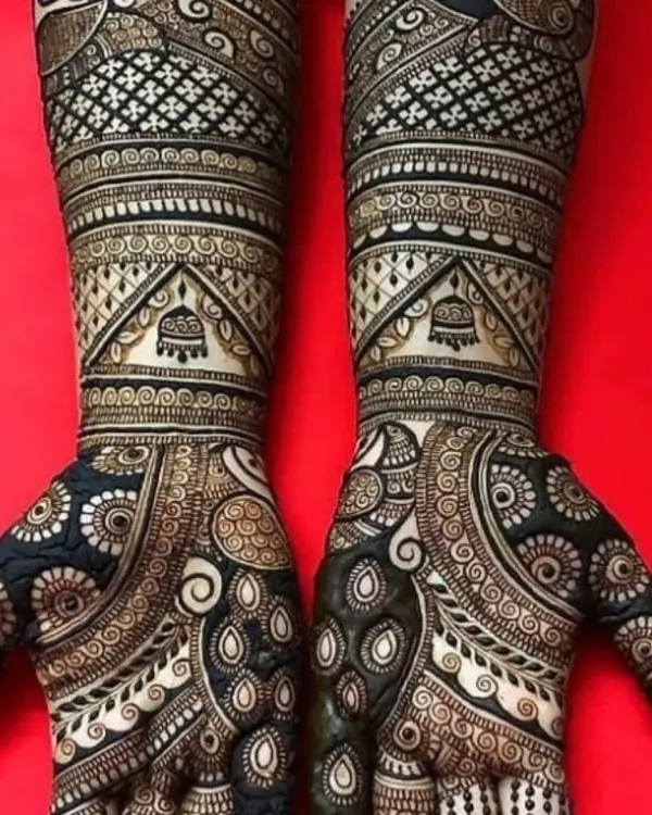 This is a classic example of full coverage mehndi. The design is packed with intricate details, including jaal work, peacock feather patterns, and hanging jhumka motifs.