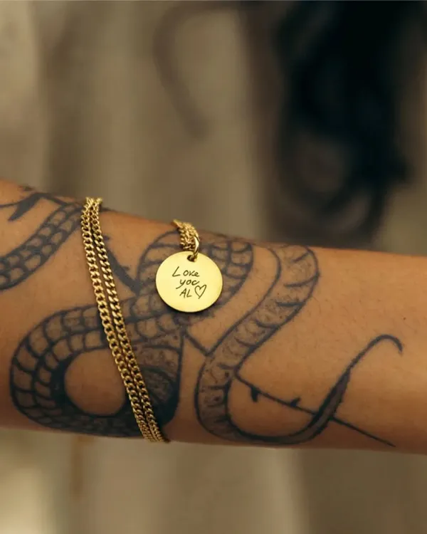 This gold round pendant features a custom engraving of a handwritten message, "Love you, Al," displayed against a tattooed arm. It's a beautiful example of how I can preserve a personal touch forever.