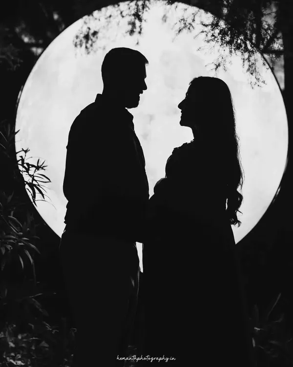 A quiet moment for expecting parents, captured in a dramatic silhouette against a full moon backdrop. This artistic, black and white maternity portrait focuses on the connection and anticipation between the couple.