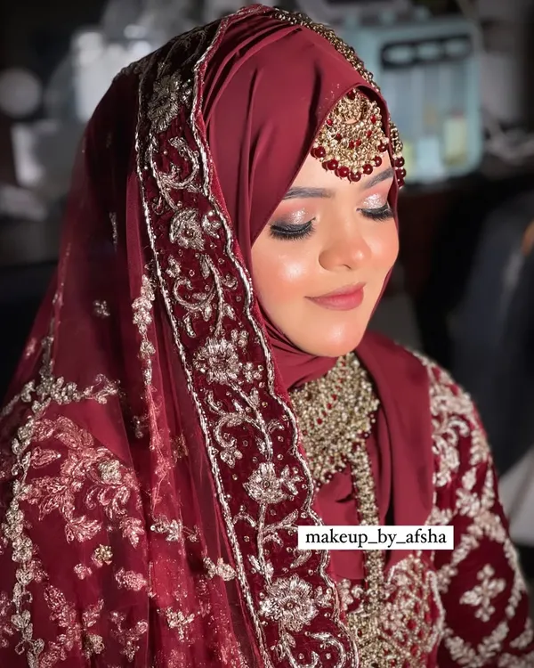 A beautiful Hijabi bride in a deep maroon outfit. The hijab is styled to perfection, and the makeup features a soft, glittery eye and a matching lip color. Mashallah, she looked so elegant.