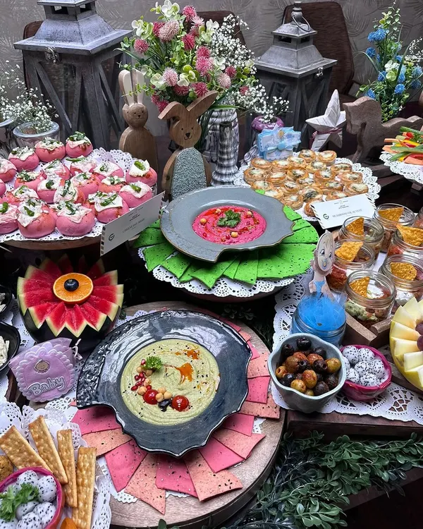 A whimsical baby shower spread with a woodland theme, featuring bunny figurines and floral arrangements. The table is laden with colorful dips, fresh fruits, and bite sized appetizers, creating a magical atmosphere.