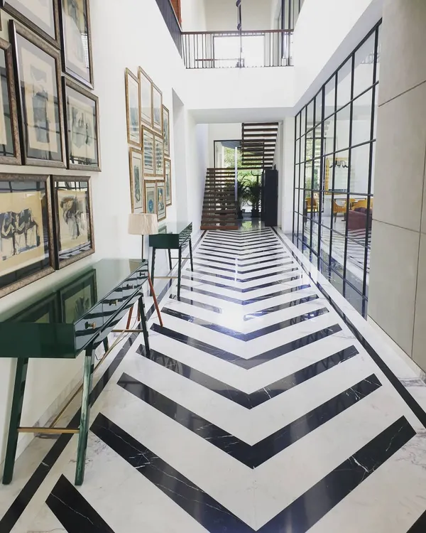 This striking chevron floor pattern, created with contrasting black and white marble, makes a bold statement in a double-height corridor. The design guides the eye through the space, enhanced by natural light from the large glass partition.