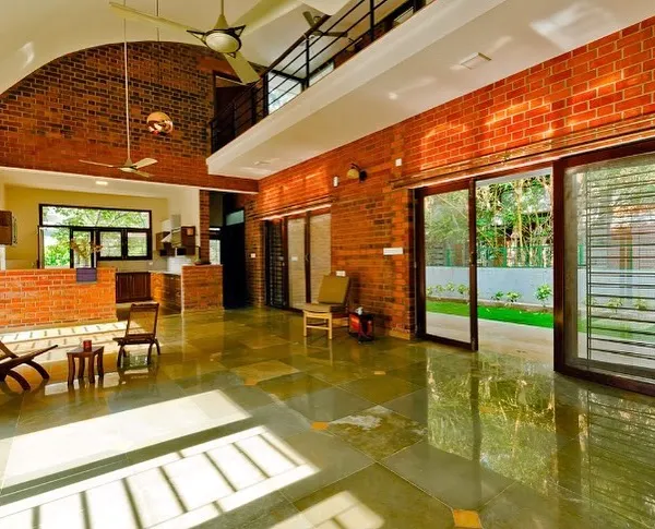 This expansive living area in the Vidyut Kapoor Residence demonstrates our use of honest materials like exposed brick and stone flooring. The double-height vaulted ceiling and large glass doors flood the space with natural light, seamlessly connecting the interior with the garden outside.